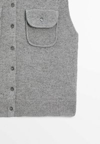 Gilet gris en maille boutonné avec ourlet côtelé et une unique poche à rabat sur la poitrine, fermée par un bouton.