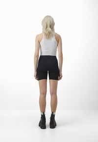 Svarta cykelbyxor med hög midja, i kombination med en figursydd vit ribbad tanktop. Modellen bär svarta kängor med en enkel design.