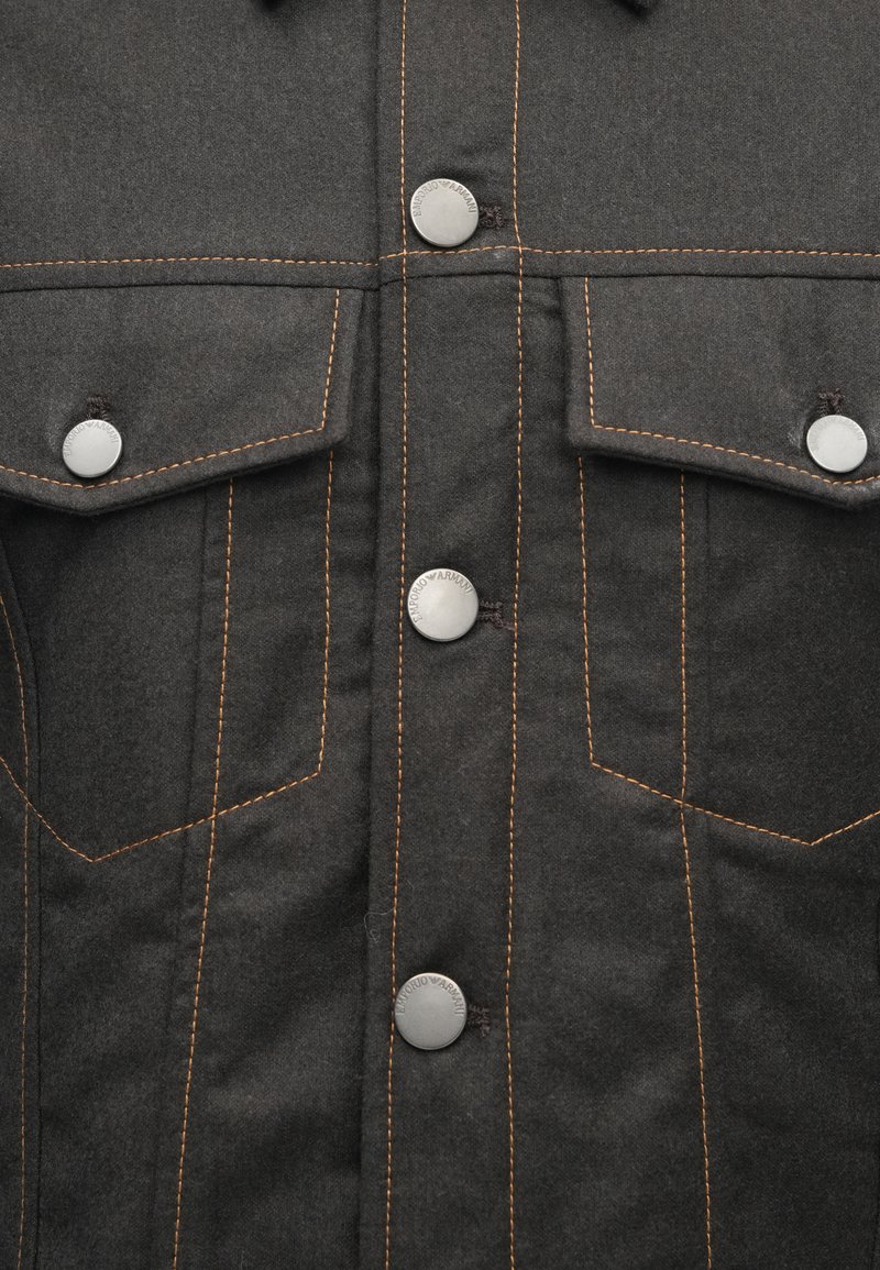 Sort denimjakke med to brystlommer, sølvfarvede knaplukninger og kontrastfarvet orange stikning overalt. Glat tekstur.