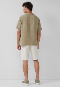 Kurzärmliges, olivgrünes strukturiertes Hemd mit Kragen. Getragen mit hellbeigen Shorts und grau-grünen Sneakers. Rückansicht gezeigt.