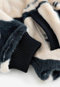 Kunstkarusnahast jakk, millel on beeži ja marine sinise sektsioonid, soonikkoes mustad mansetid, pehme tekstuur ja kontrastsete värvimustritega.