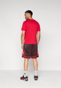 Κόκκινο βαμβακερό t-shirt συνδυασμένο με μαύρο σορτς μπάσκετ με κόκκινες λωρίδες και λεπτομέρειες, φορεμένο με μαύρα και κόκκινα αθλητικά παπούτσια.