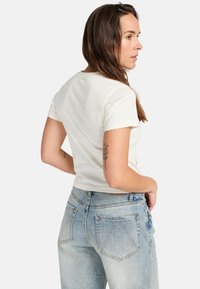 T-shirt blanc à manches courtes, design ajusté, en coton doux. Porté avec un jean taille haute bleu clair avec des poches arrière et un délavage.