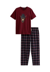 Burgundy kortärmad skjorta med en höglandsko som bär en marinblå pom-pom mössa, tillsammans med marinblå, burgundy och vita rutiga byxor.