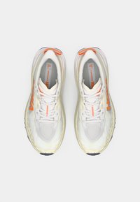 Baskets de course blanches et gris clair avec une tige en maille texturée, des accents réfléchissants, un logo orange et une semelle épaisse et rembourrée.