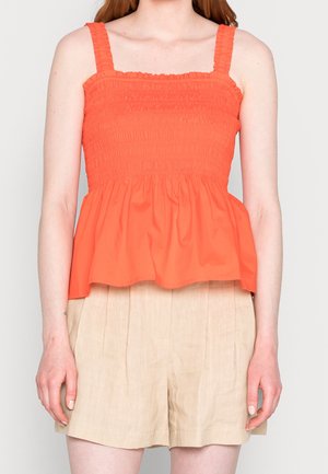 Haut peplum à smocks orange avec de larges bretelles, présentant un corsage texturé et une jupe fluide. Associé à un short plissé beige clair.