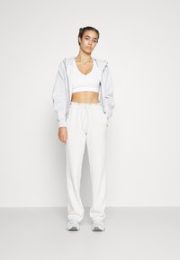 Šedá mikina na zip, bílý crop top a světle béžové tepláky. Pohodlný střih s elastickým pasem, doplněný šedými sportovními botami. Jednoduchý design.