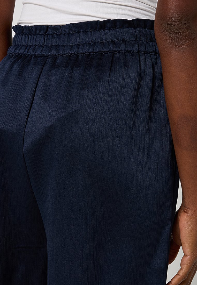 Marineblaue, gerippte Sweatpants mit elastischem Taillengummi, die eine glatte Textur und eine lockere Passform aufweisen. Seitliche Nähte sichtbar am Bein.