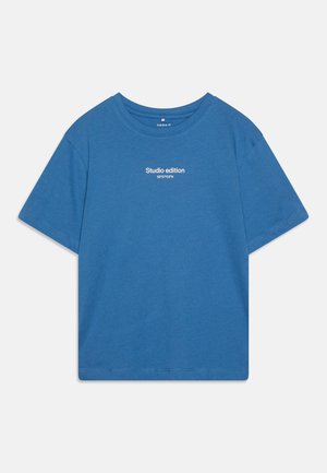 Sininen puuvillapaita lyhythihaisilla, pyöreällä pääntiellä ja valkoisella "Studio edition" -tekstillä edessä. Sileä rakenne, normaali istuvuus.