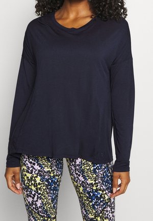 Person wearing a loose-fitting, long-sleeve navy top and patterned leggings with yellow, blue, black, and white floral design.