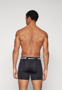 Black Nike boxer briefs with a white logo on the elastic waistband, fitted design, and smooth texture. Back view showcases the shorts' length and fit.