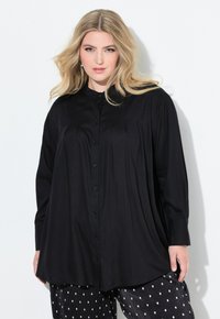 Camicia nera con bottoni, a maniche lunghe, realizzata in un tessuto liscio. Presenta una vestibilità rilassata e un leggero svaso sull'orlo. Abbinate a pantaloni a pois.