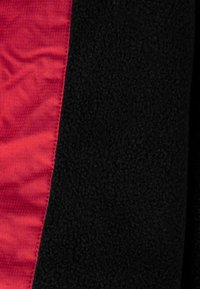 Czerwone i czarne sekcje tkaniny, charakteryzujące się gładką satynową fakturą oraz puszystym czarnym polarem. Widoczne kontrastowe szwy wzdłuż szwu.