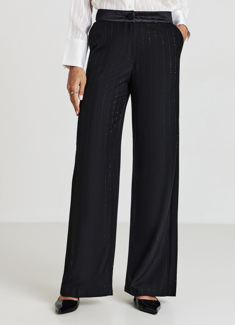 Pantalons larges noirs avec des rayures verticales brillantes, ceinture en satin et fermeture à bouton. Tissu lisse avec un design fluide.
