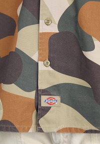 Kurzarmhemd mit einem mehrfarbigen abstrakten Muster in Braun, Olivgrün und Beige. Enthält Knöpfe und ein "Dickies"-Label.