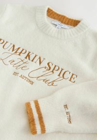 White knit sweater with "Pumpkin Spice Latte Club" and "Est Autumn" in orange, plus orange-striped cuffs and ribbed collar.