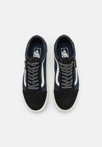 Sapatilhas de tecido azuis com biqueira de camurça preta, faixa lateral branca e atacadores em padrão preto e branco sobre um fundo branco.