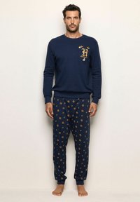 Conjunto de sudadera y pijama en azul marino. La sudadera cuenta con bordado dorado. Los pantalones de pijama tienen un patrón con pequeños iconos sobre un fondo oscuro.