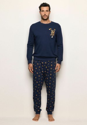 Conjunto de sudadera y pijama en azul marino. La sudadera cuenta con bordado dorado. Los pantalones de pijama tienen un patrón con pequeños iconos sobre un fondo oscuro.