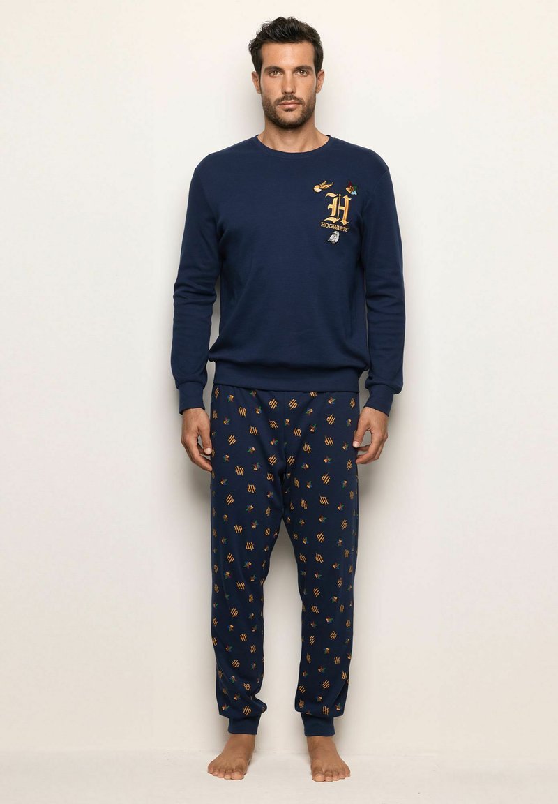 Conjunto de sudadera y pijama en azul marino. La sudadera cuenta con bordado dorado. Los pantalones de pijama tienen un patrón con pequeños iconos sobre un fondo oscuro.