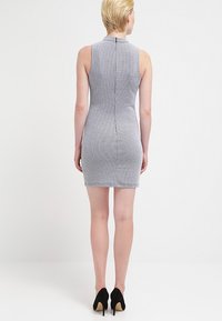 Szara, bezrękawnikowa mini sukienka z teksturowanej tkaniny i pionowym zamkiem z tyłu, noszona z czarnymi szpilkami.