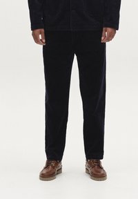 Marineblauwe corduroy jas met knoopsluiting, voorzakken, gecombineerd met bijpassende corduroy broek en bruine leren schoenen met een gestructureerde zool.