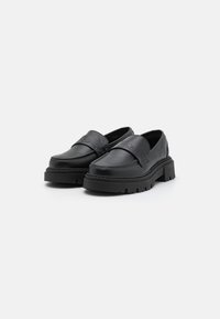 Juodos odinės slip-on tipo bateliai su masyviu guminiu padu, su lygiu paviršiumi ir išgaubtu žvaigždės motyvu ant priekinio dirželio.