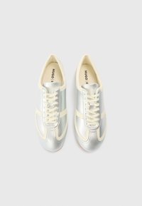 Ténis desportivos, parte superior sintética prateada com detalhes em creme, biqueira arredondada, atacadores e detalhes do logótipo na língua. Sola de borracha.