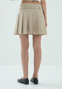 Beżowa, mini spódnica w plisy z płaskim pasem i bocznymi kieszeniami. Lekki materiał o miękkiej teksturze, zaprojektowany z myślą o dopasowanym kroju.