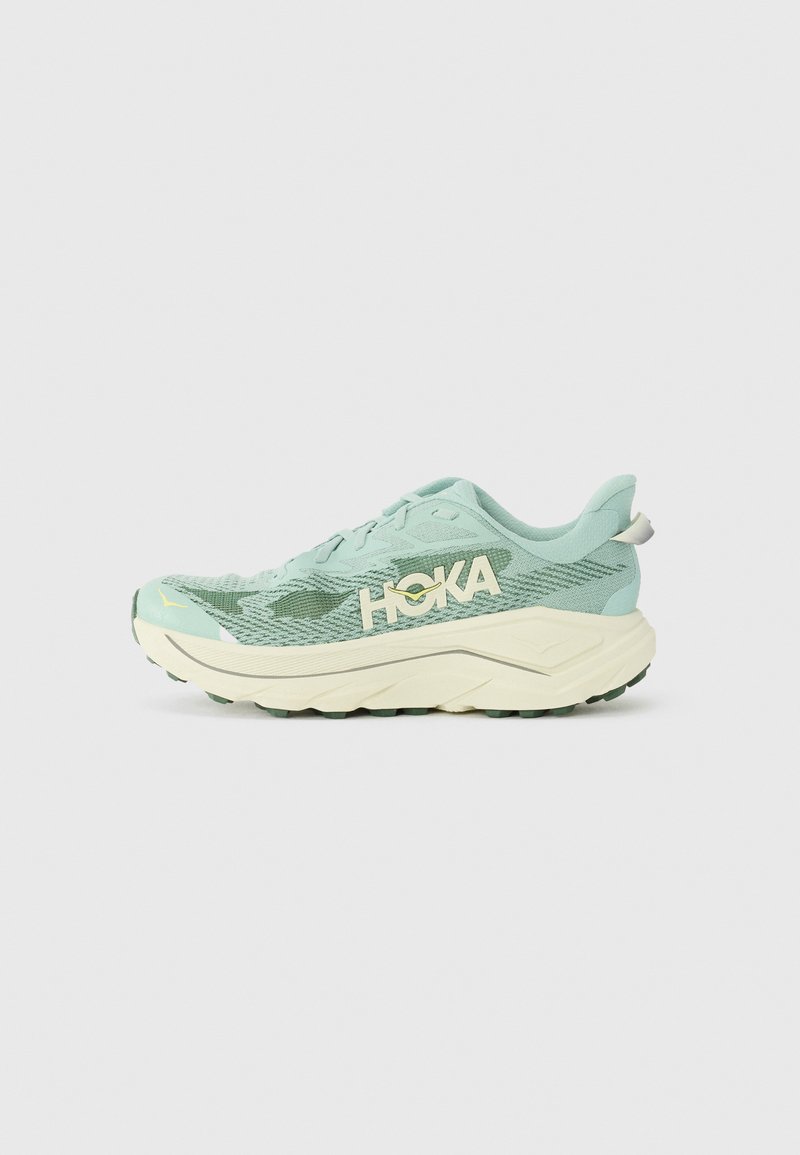 Hellgrüner Laufschuh mit strukturiertem Mesh-Obermaterial, dicker cremefarbener Zwischensohle und grüner Gummisohle. HOKA-Logo in creme an der Seite.
