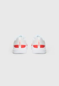 Hvide sneakers med røde detaljer og "KOURTFLY" tekst. Har en glat overflade, rund form og en polstret sål med en lys blå foring.