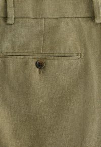 Olivovo zelená látka s textúrovaným povrchom, vybavená jedným zadným vreckom so zapínaním na hnedé gombíky. Strihaný dizajn bez viditeľných vzorov.