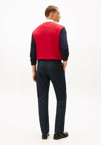 Rood en marineblauw langemouwen overhemd met een witte kraag, gecombineerd met donkerblauwe broeken. Het overhemd heeft een effen achterkant en een V-stiksel detail.
