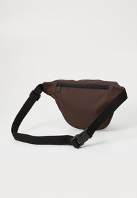 Braune Gürteltasche aus strukturiertem Material mit geschwungenem Design. Verfügt über eine Reißverschlusstasche und einen verstellbaren schwarzen Gurt mit einem Clip.