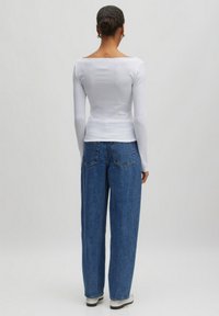 Weißes Langarmoberteil mit quadratischem Ausschnitt, kombiniert mit hoch-taillierten, locker sitzenden blauen Jeans aus verblichenem Denim.