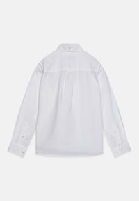 Chemise blanche à manches longues en tissu léger. Elle présente un col rabattu, des poignets boutonnés et un détail de pli dans le dos.