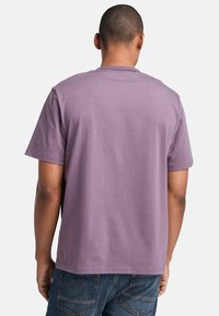 Fialové tričko s krátkým rukávem a kulatým výstřihem. Měkká látka s hladkým povrchem. Spodní lem je rovný, v kombinaci s modrými džíny.