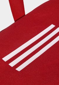 Bolso de tela roja con una superficie texturizada, con tres franjas blancas paralelas y una correa roja a juego.
