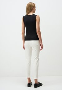 Top nero senza maniche con un design aderente, abbinato a pantaloni bianchi slim-fit e scarpe nere basse, visto da dietro.