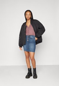 Black bomber jacket over a maroon buttoned top, paired with a blue denim skirt featuring front buttons and black lace-up boots.