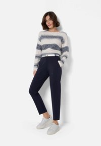 Maglione a righe crema e blu navy con scollo rotondo abbinato a pantaloni navy eleganti. Sneakers bianche completano l'outfit.