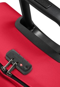 Maleta roja con un acabado texturizado, mango negro retráctil y un mecanismo de cierre que incluye cremalleras plateadas y una cerradura de combinación.