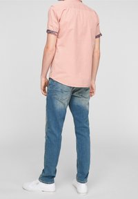 Světle růžová krátká košile s vzorovanými manžetami, kombinovaná s vybledlými modrými džíny a bílými teniskami, pohled zezadu.