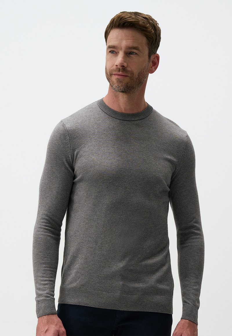 Pull en maille gris avec des manches longues, un col rond et des poignets côtelés. Le tissu a une texture lisse, un design ajusté et un motif subtil.
