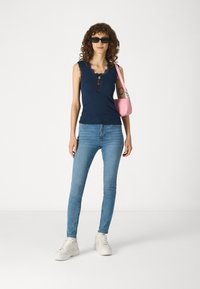 Ναυτικό αμάνικο μπλουζάκι με δαντέλα, ανοιχτό γαλάζιο skinny τζιν, λευκά αθλητικά παπούτσια με πλατφόρμα και μια μικρή ροζ τσάντα. Μαύρα γυαλιά ηλίου.