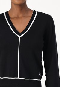 Maglione nero a maglia con scollo a V, dettagli in bianco lungo lo scollo e l'orlo, e una silhouette aderente con texture a coste.