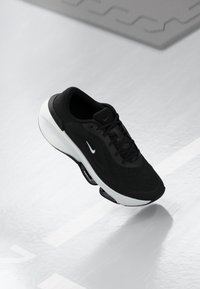 Scarpa sportiva nera con tomaia in maglia testurizzata, logo Swoosh bianco e una robusta suola intermedia bianca, dotata di distintivi elementi ammortizzati a molla.