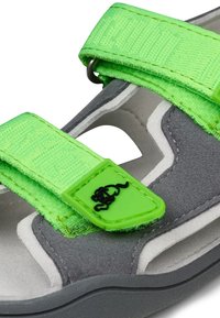 Sandalo in suede grigio con fasce in tessuto verde brillante, con dettaglio del logo e chiusure in velcro. La suola è sagomata e testurizzata.