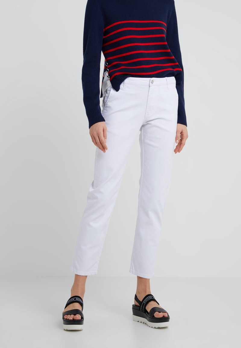 Pantalon en denim blanc à coupe droite, associé à un pull marine rayé avec des lignes rouges et des détails sur les côtés. Des sandales à plateforme complètent la tenue.