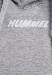 Grå sweatshirt i ett mjukt, texturerat material. Har en stor, vit logotyp "HUMMEL" iögonfallande placerad på framsidan.